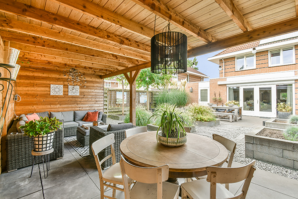 modern and tropical outdoor dining space. a patio with chairs, tables and plants on the table in front of an outdoor living room that has wood paneled walls