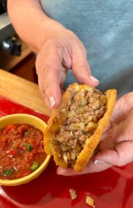 Dressing a gordita stuffed with refried beans and red chile beef picadillo.