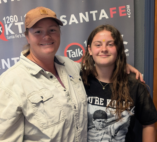 Two smiling people pose together in front of a radio station backdrop with SantaFe logos and branding.
