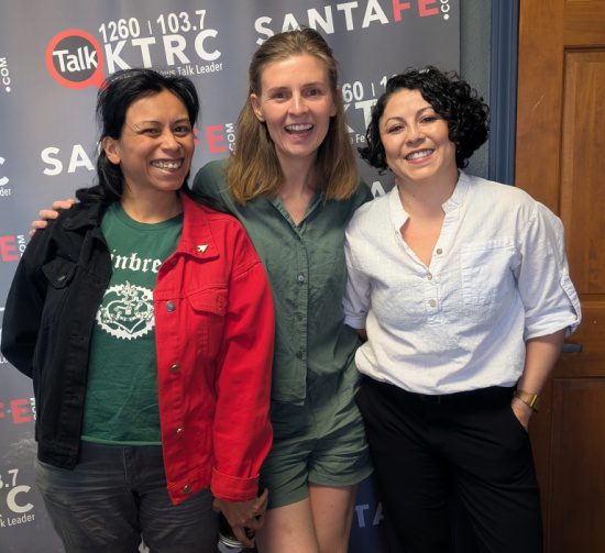 Three women posing together in front of a Talk KTRC radio backdrop, smiling at the camera.