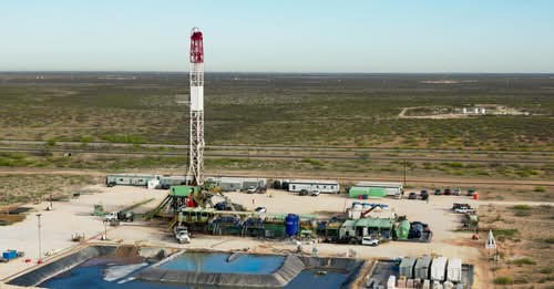 Oil drilling rig in a desert site with support vehicles and water tanks nearby.