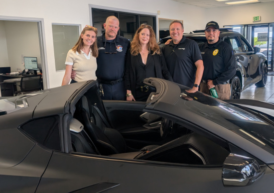 Five people pose for a group photo in a car showroom beside two black convertible sports cars.